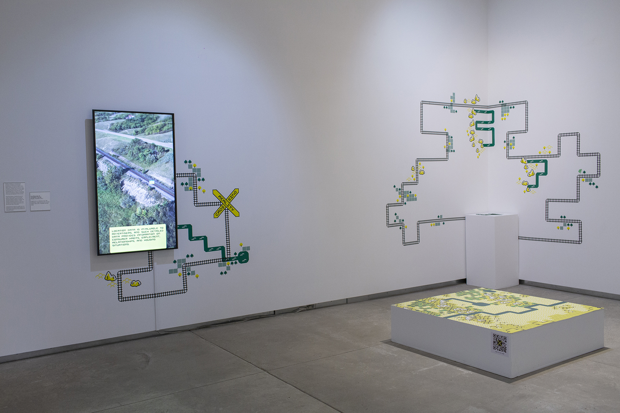 Indoor installation of Reality Crossing at InterAccess, featuring an augmented reality map, vinyl applications, zines on a plinth, and a single-channel video.